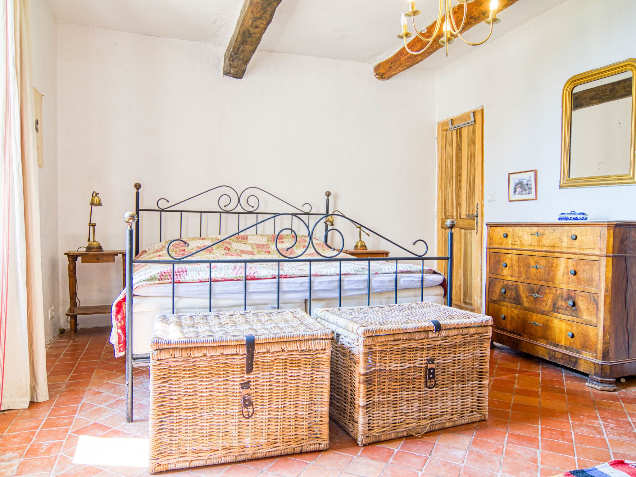 A bedroom with a metal bed frame, wooden dresser, wicker baskets, and a wooden door.