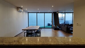 Amplia sala de estar con mesa y sillas de madera, un ventanal con vistas y un diseño moderno de techo.