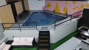 Un área de piscina en la azotea con un jacuzzi, sillones de descanso y una escalera que lleva a un nivel superior.