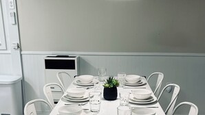 A dining table set with white plates, glasses, and cutlery, surrounded by white chairs, with a pendant light above. - HOT TUB, beach access, 2-bdrm cottage just outside Port Austin with AC & WiFi #1 (Port Austin)