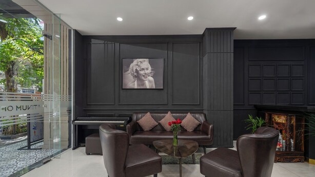 A modern living room with a dark brown leather sofa, two leather armchairs, a glass coffee table with a vase of red flowers, and a framed picture on the wall. - Platinum Orchid Hotel Danang (Da Nang)