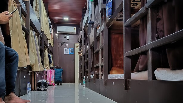 A corridor with metal lockers on both sides, a tiled floor, and a person sitting on the floor. - ASRA DORMITORY  (Mumbai)