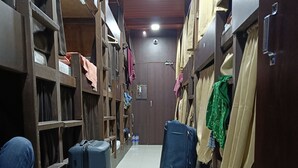 A narrow hallway with wooden lockers on both sides, a tiled floor, and a few pieces of luggage. - ASRA DORMITORY  (Mumbai)