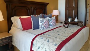 Cama bem arrumada com colcha estampada, cabeceira de madeira e mesa de cabeceira com abajur e cafeteira.