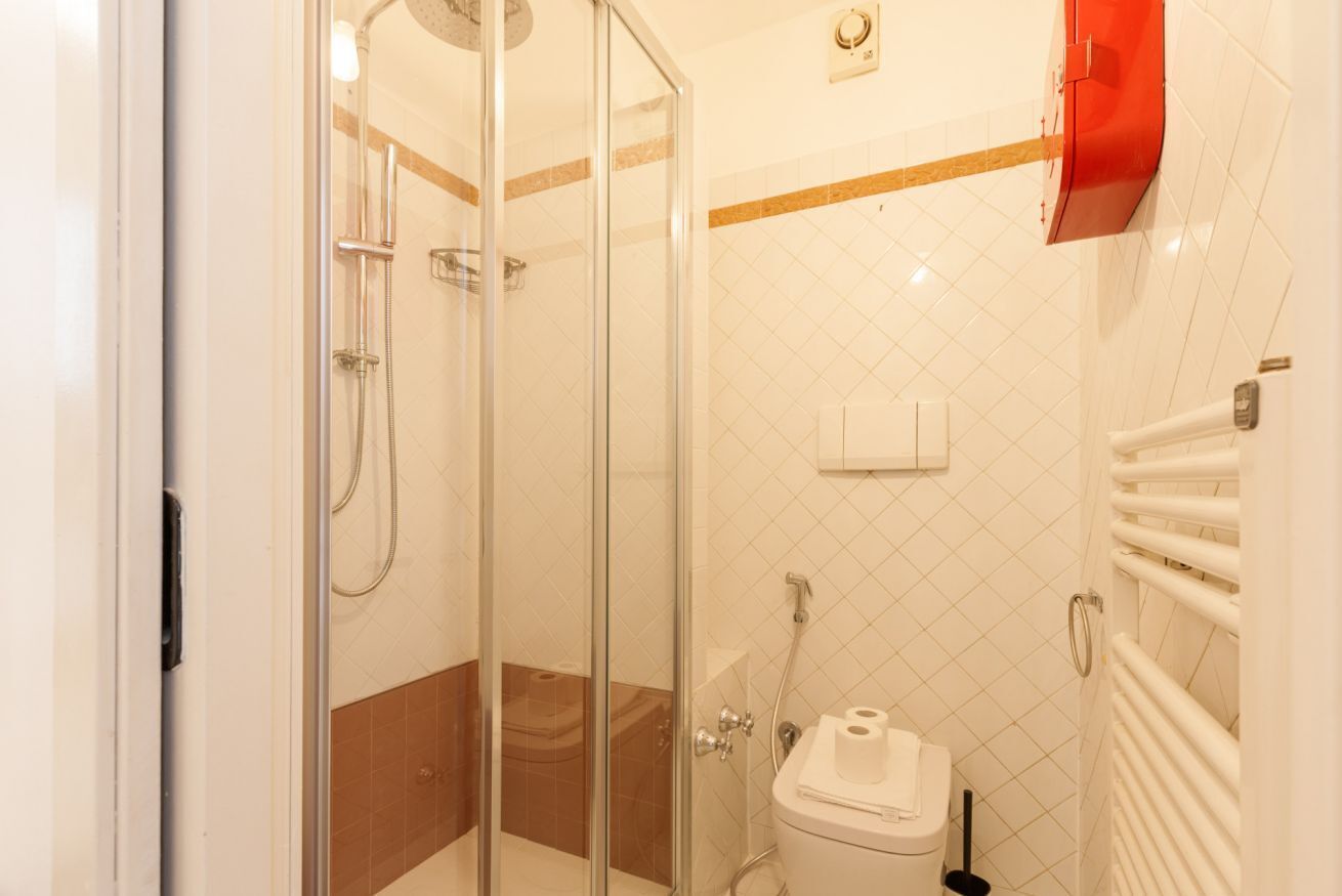 A bathroom with a glass-enclosed shower, a toilet, and a towel rack.