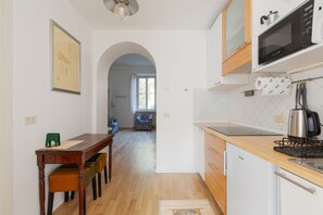 A modern kitchen with a microwave, kettle, and a small refrigerator. There is a dining area with a wooden table and chairs. - Cozy 55 m2 apartment for 4 people, located on the 3rd floor of a building with lift a few steps from the suggestive area of ​​Isola, where tradition meets innovation, but also from the picturesque China Town of via Paolo Sarpi, from the Monumental Ce (Milano)