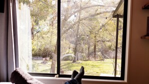 A room with a large window overlooking a yard with trees and a swing set. - Romantic tiny house escape amongst wineries & MTB Trails. Fire Pit, Creekside (Lidster)