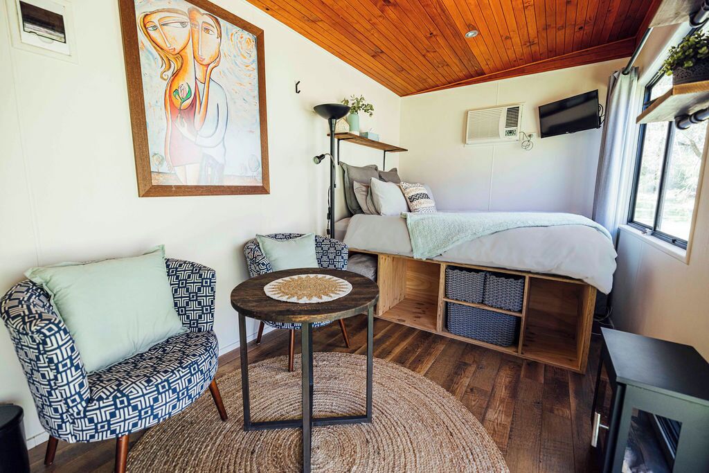 Um quarto aconchegante com uma cama, uma cadeira, uma mesinha e um quadro na parede.