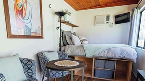 Um quarto aconchegante com teto de madeira, uma cama, um sofá, uma mesa redonda pequena e um quadro na parede.
