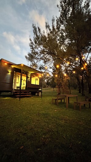 Une cabane rustique dotée d’un porche, entourée d’arbres et bordée d’une pelouse.