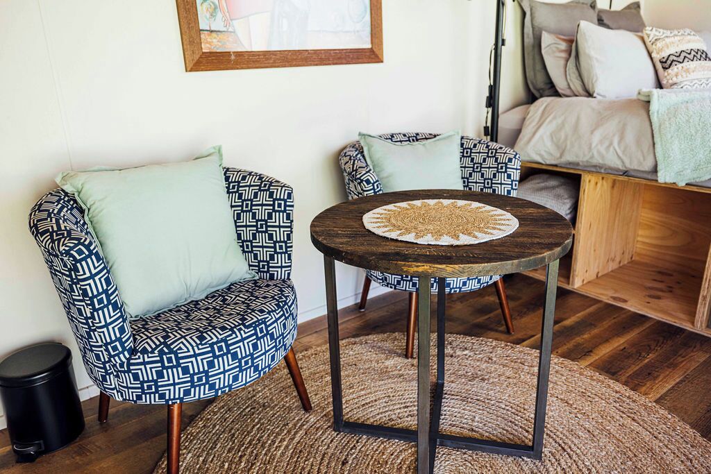 Un salon chaleureux avec deux fauteuils à motifs, une petite table ronde surmontée d’un set de table en fibres tressées et un canapé agrémenté de coussins.
