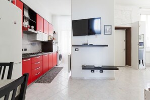 A modern kitchen with red cabinets, a built-in stove, and a flat-screen TV mounted on the wall.