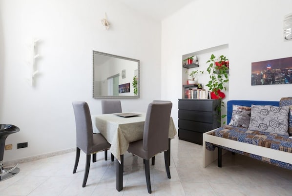A dining area with a table and chairs, a sofa, a bookshelf, and a mirror on the wall.