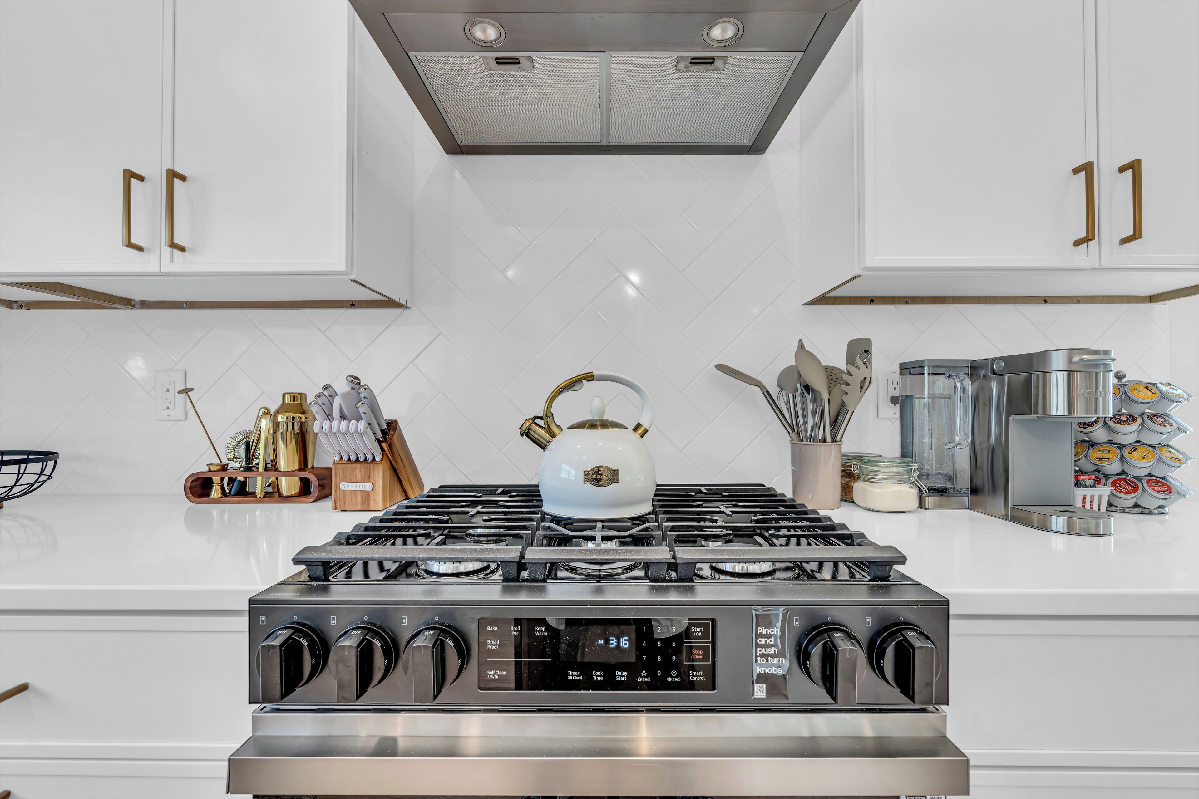 Una cocina moderna con armarios blancos, estufa de acero inoxidable y diversos utensilios de cocina.
