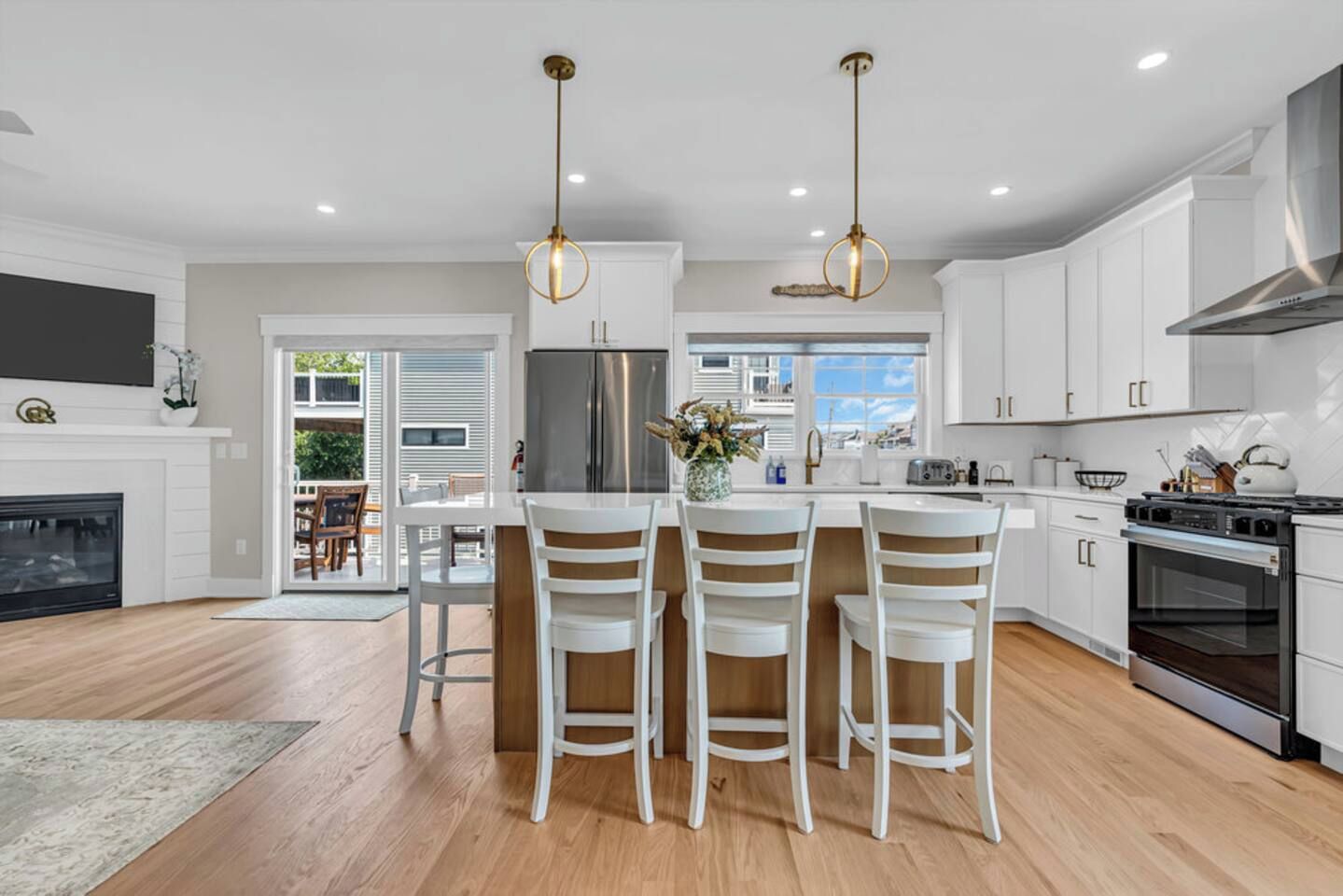 A modern kitchen with white cabinetry, a stainless steel refrigerator, and a gas stove. There are two pendant lights above the island.