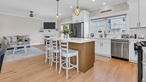 A modern kitchen with white cabinetry, a central island with bar stools, stainless steel appliances, and pendant lighting. - Professionally Managed | 1 Block to Beach (Seaside Park)
