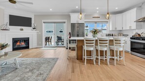 A modern kitchen with white cabinetry, a central island with bar stools, a built-in oven, and a stainless steel refrigerator. - Professionally Managed | 1 Block to Beach (Seaside Park)