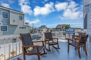 A balcony with wooden rocking chairs, a grill, and a view of neighboring houses. - Professionally Managed | 1 Block to Beach (Seaside Park)