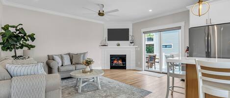 A modern living room with a fireplace, a dining area, and a kitchen with a stainless steel refrigerator.