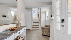 A hallway with a staircase, a patterned armchair, and a large mirror. - Professionally Managed | 1 Block to Beach (Seaside Park)