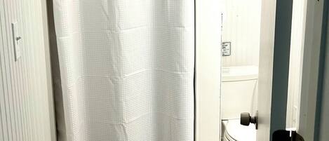 A bathroom with a white shower curtain, a toilet, and a door with a handle.