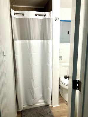 Un baño con cortina de ducha blanca, un inodoro y una puerta con pomo.
