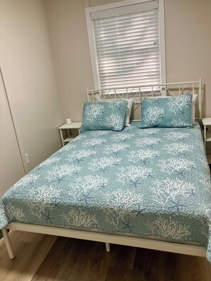 Un dormitorio con una cama, dos mesitas de noche y una ventana con persianas.