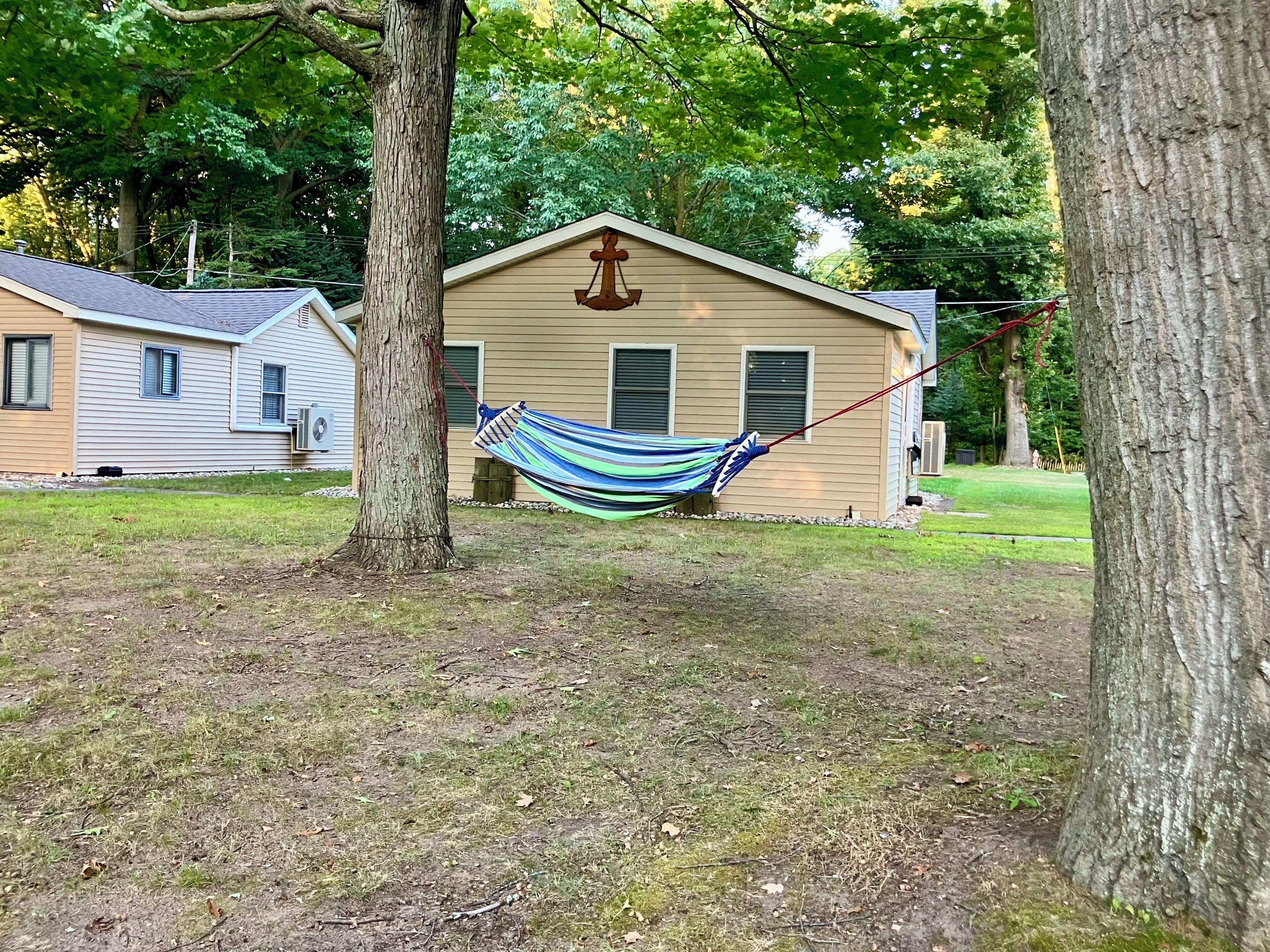 A hammock tied between two trees in a grassy area with a house in the background.