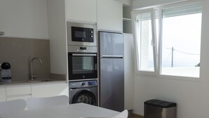 A modern kitchen with a microwave, oven, and refrigerator. There is a dining table with chairs and a washing machine.