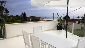 A rooftop terrace with a white table and chairs, a potted plant, and a white umbrella.