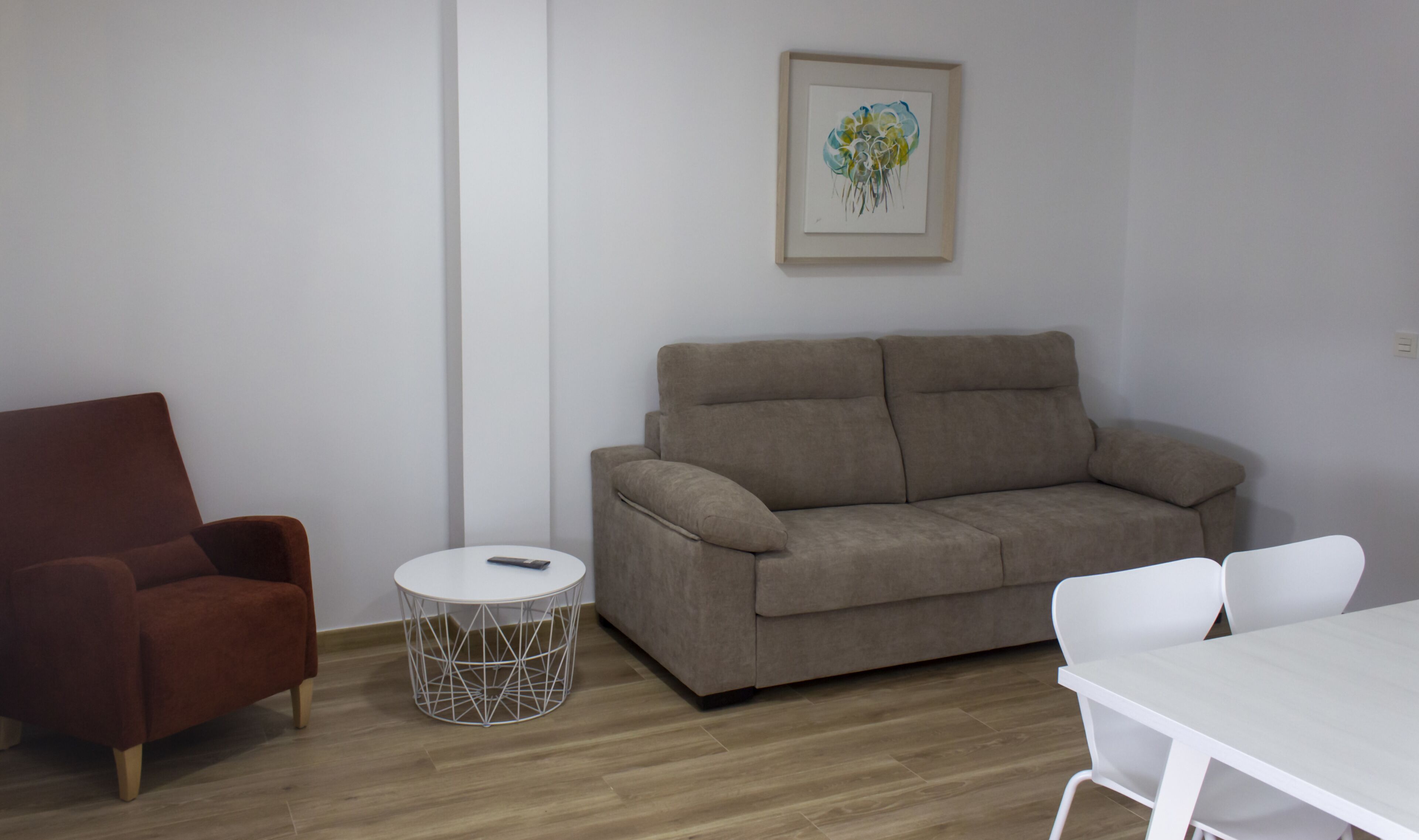 Ett vardagsrum med en brun soffa, en röd fåtölj, ett vitt bord och ett runt soffbord med ett geometriskt underrede.