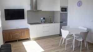 Cozinha moderna com televisão de tela plana, eletrodomésticos de aço inoxidável e área de refeições com cadeiras brancas.