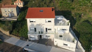 Um edifício de dois andares com telhado de telhas vermelhas, uma varanda com área de estar externa e uma placa com a inscrição "ALEN DE LOURO".