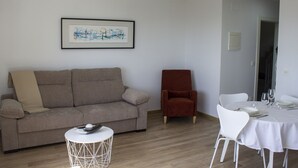 A living room with a sofa, a red armchair, a round coffee table, and a dining table set for four.