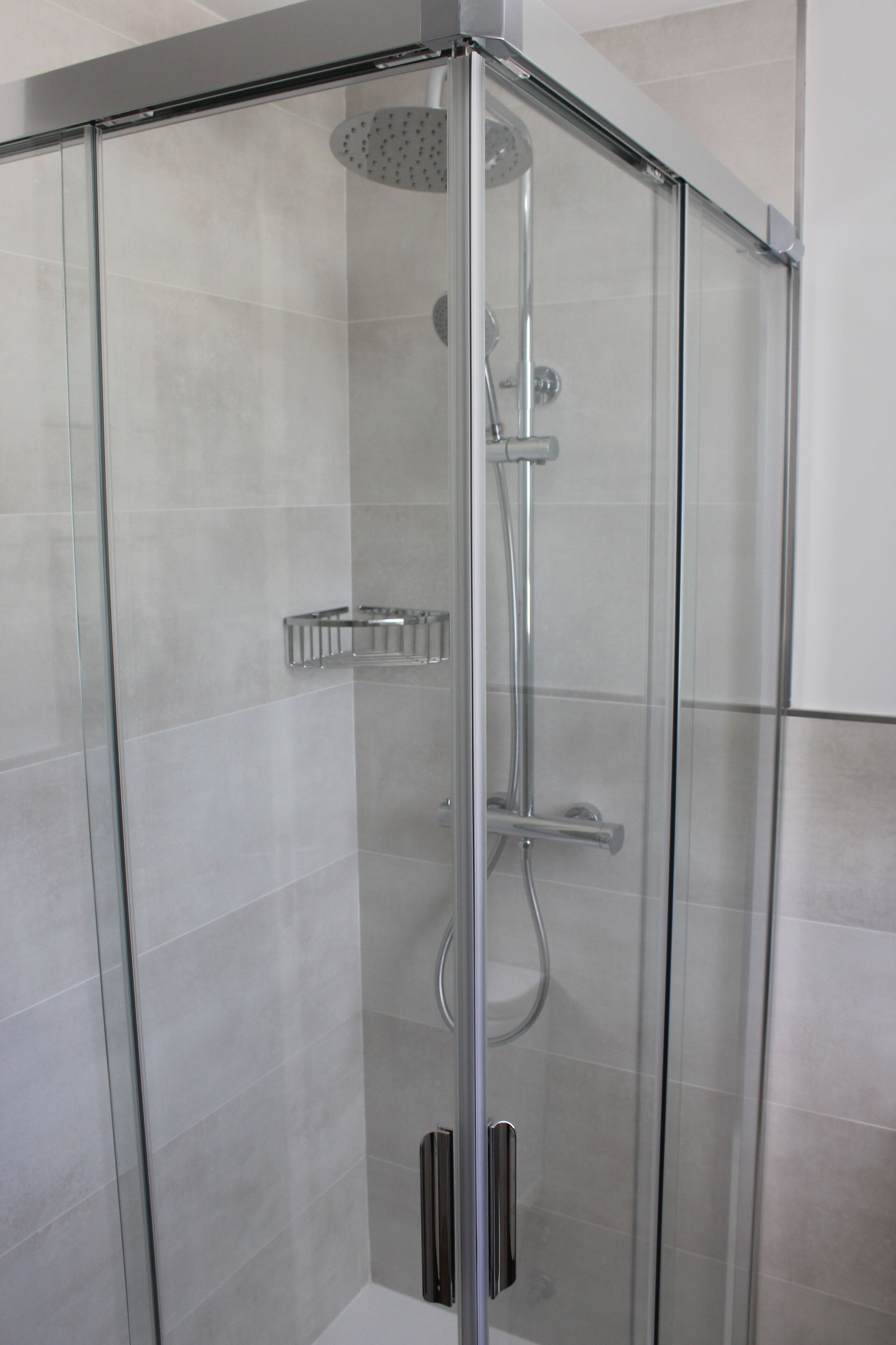 A glass-enclosed shower with a handheld showerhead and a wall-mounted faucet.