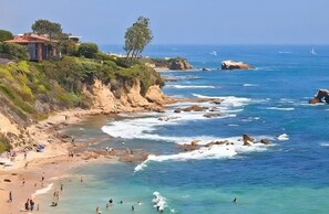 A coastal beach scene with rocky cliffs, clear blue waters, and a few people enjoying the beach. - Ultimate Newport Beach Retreat - #California (Newport Beach)