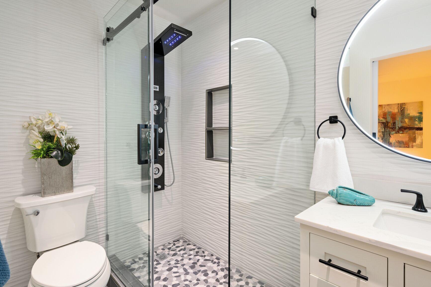 Un baño moderno con cabina de ducha de vidrio, inodoro, lavamanos con espejo y una planta decorativa.