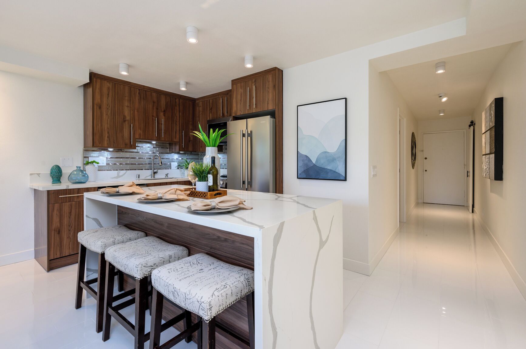 A modern kitchen with wooden cabinets, a marble island, and bar stools.