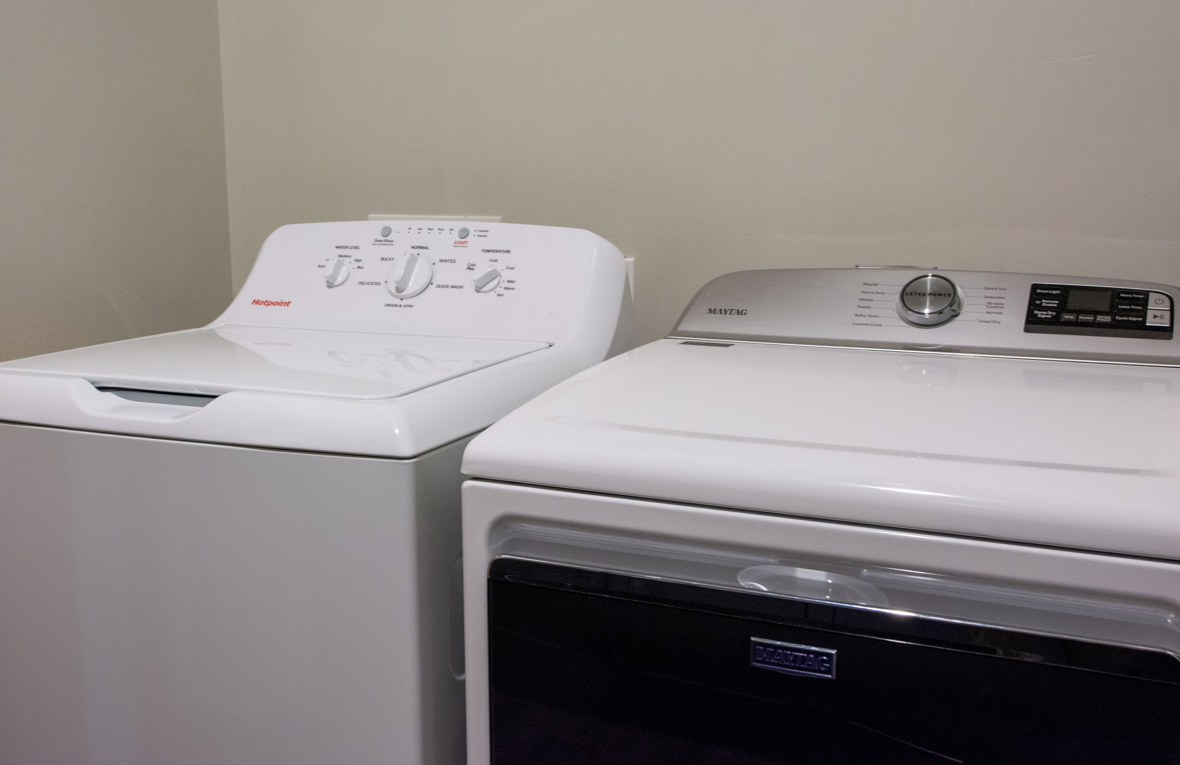 Een wasruimte met twee witte wasmachines, waarvan één van het merk Hotpoint en de andere van Mavtag.