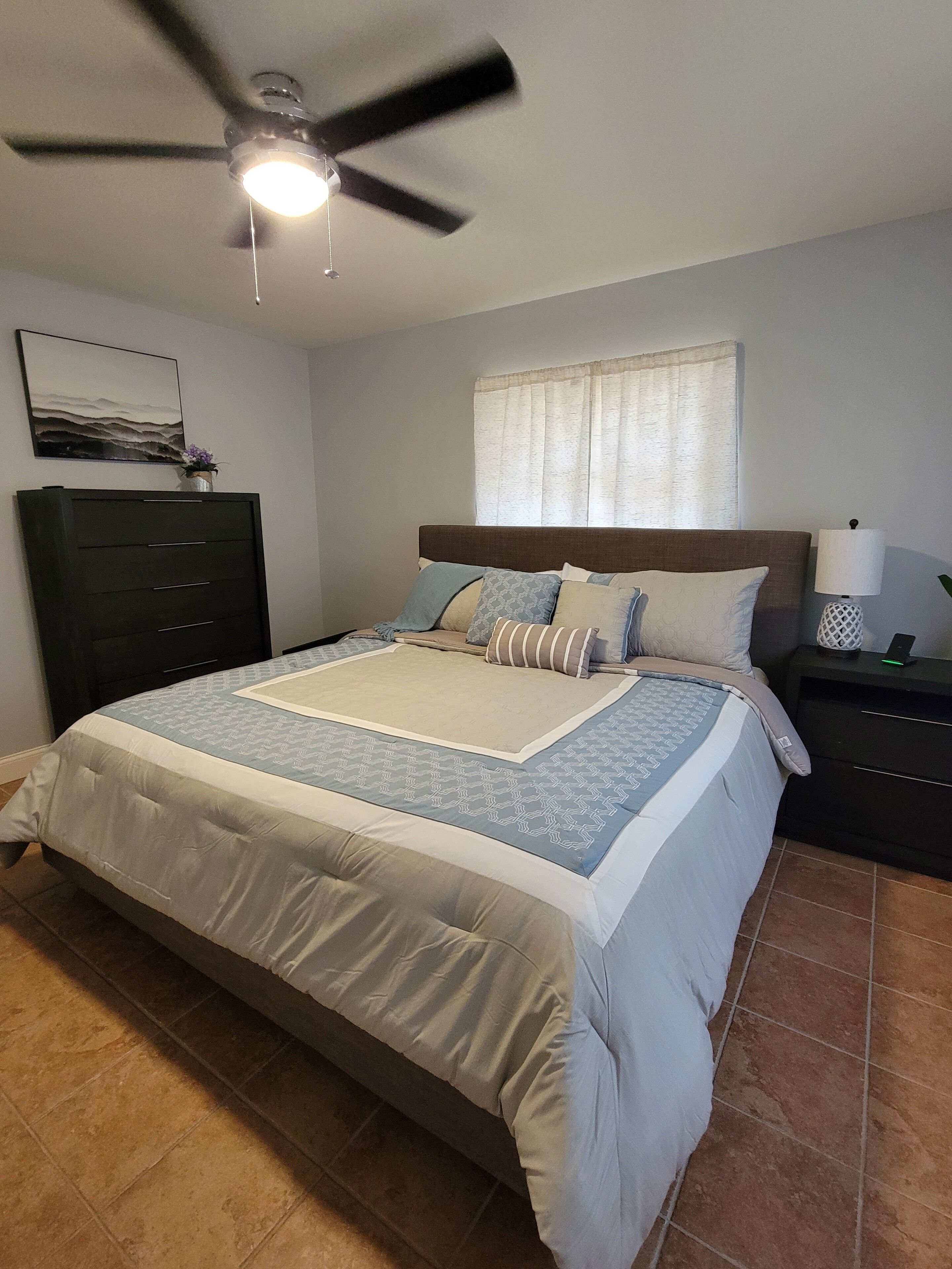 Un dormitorio con cama, ventilador de techo, mesita de noche, lámpara y cómoda.