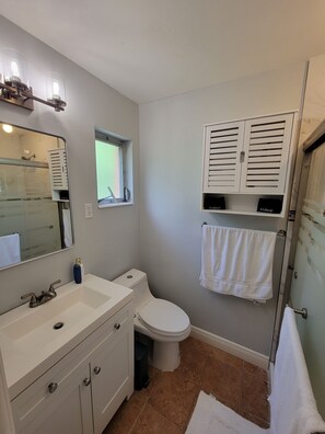 A bathroom with a white sink, vanity, and toilet. There is a window with a view of the outside, a towel hanging on the wall, and a mirror above the sink.