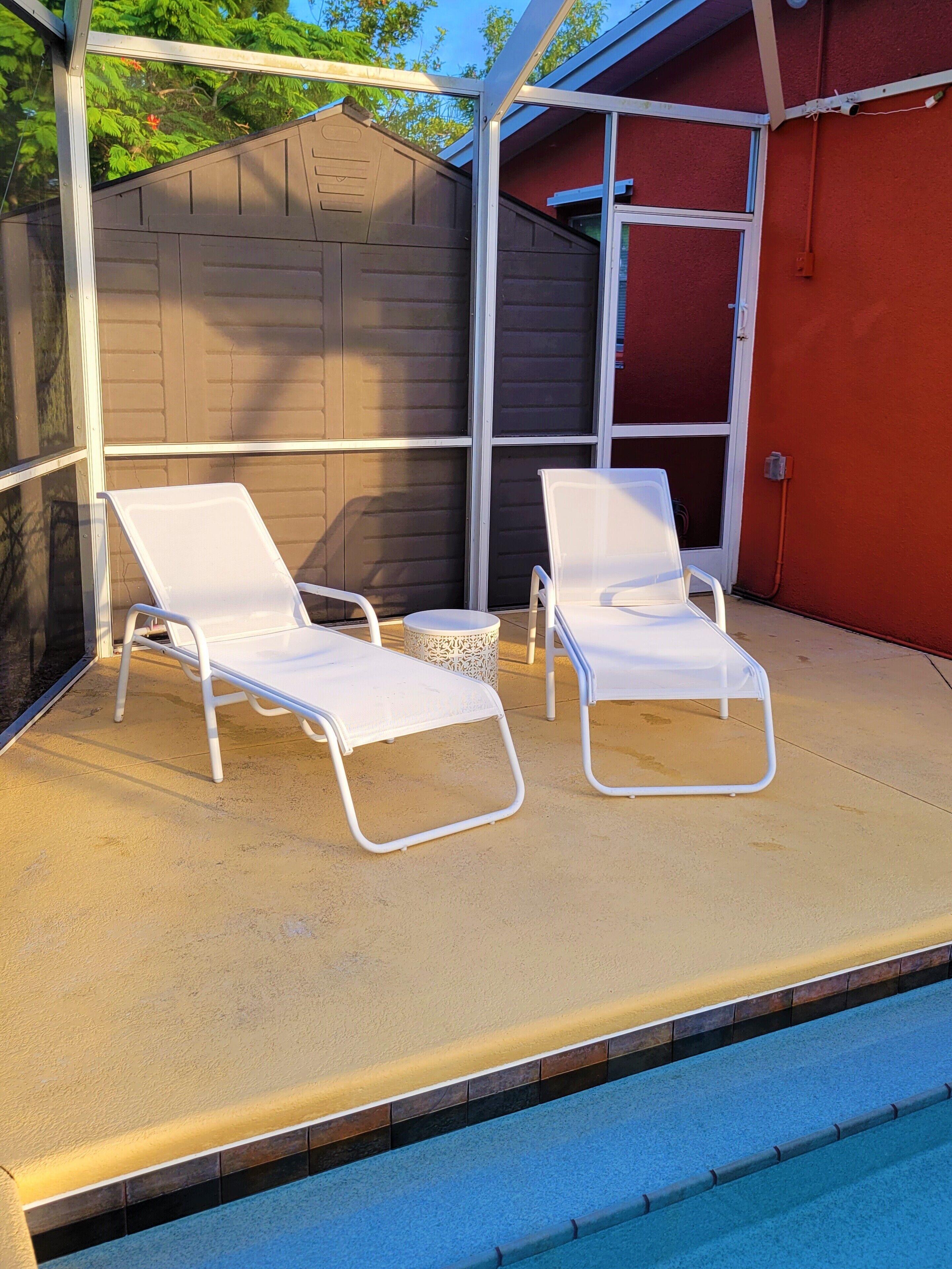 A poolside area with two white lounge chairs and a small round table.