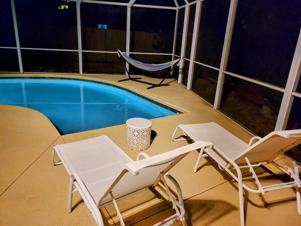 An outdoor swimming pool with white lounge chairs and a hammock.