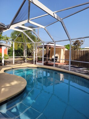 A backyard with a swimming pool, covered patio, and a wooden fence.
