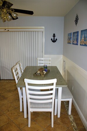 A dining area with a wooden table, white chairs, and a ceiling fan.