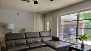 A living room with a sectional sofa, a small table with a plant, a lamp, and a window with a view of parked cars. - Spacious 4-bedroom house in tranquil Vero Beach with AC, WiFi (Vero Beach)