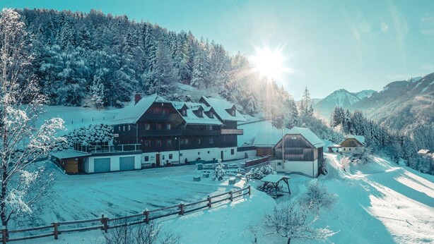 Een ruime, meerlaagse chalet met een met sneeuw bedekte dak, gelegen op een omheind perceel met een bebost berglandschap op de achtergrond.