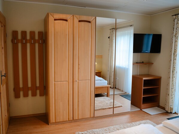 A bedroom with a large wardrobe, a bed, a TV, and a mirror.
