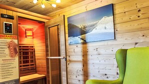 Een sauna met houten wanden, een groene stoel, een wandheater en een lijst met een foto van een besneeuwde berg.