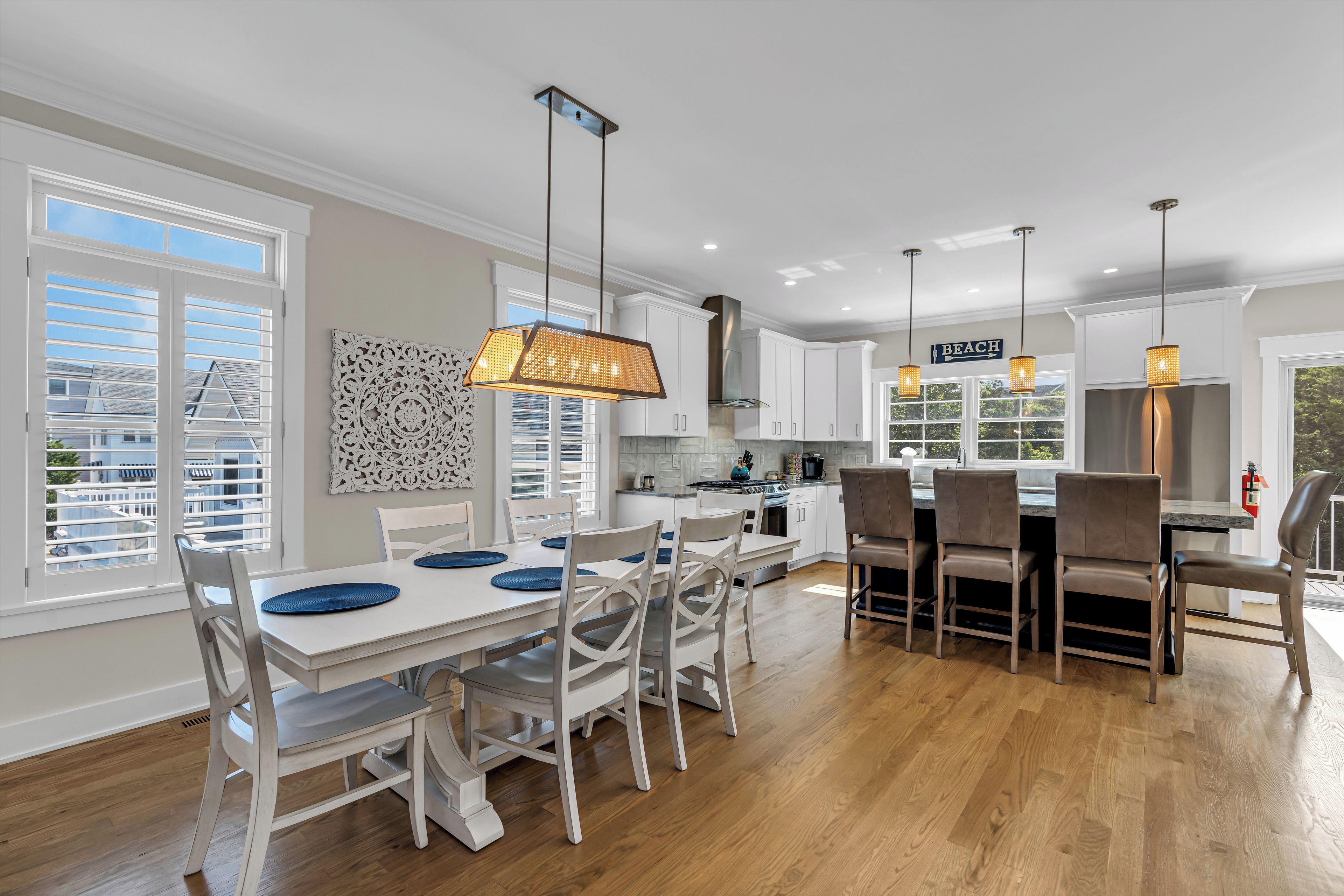 A modern kitchen with white cabinets, a dining area with white chairs, and pendant lighting.